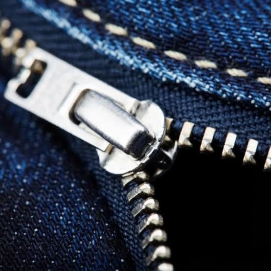 Zíper metálico durável em tecido jeans mostrando detalhes dos dentes e do cursor.